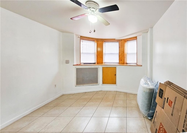 empty room with a ceiling fan, baseboards, a wealth of natural light, and light tile patterned flooring