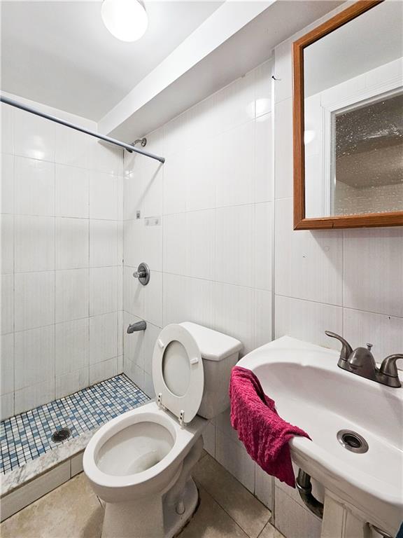 bathroom featuring tile patterned flooring, toilet, tile walls, backsplash, and a stall shower