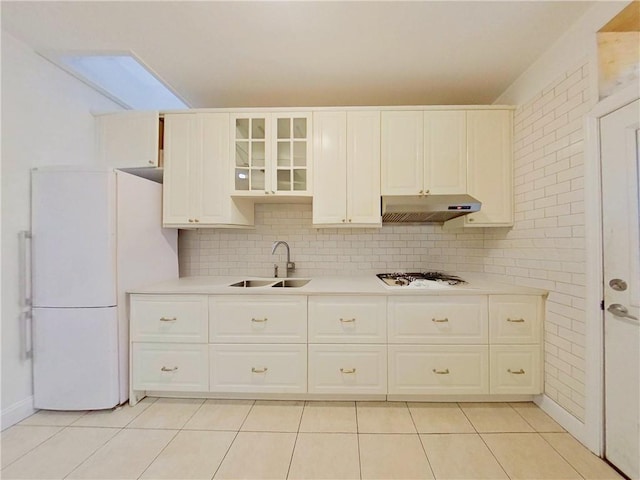 kitchen featuring light tile patterned floors, under cabinet range hood, white appliances, a sink, and light countertops