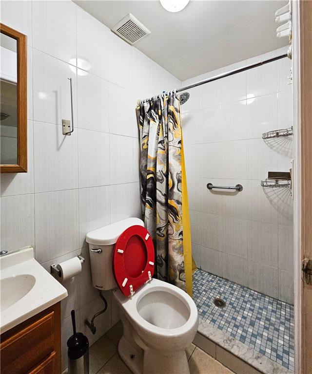 full bathroom featuring visible vents, toilet, tile patterned flooring, a tile shower, and tile walls