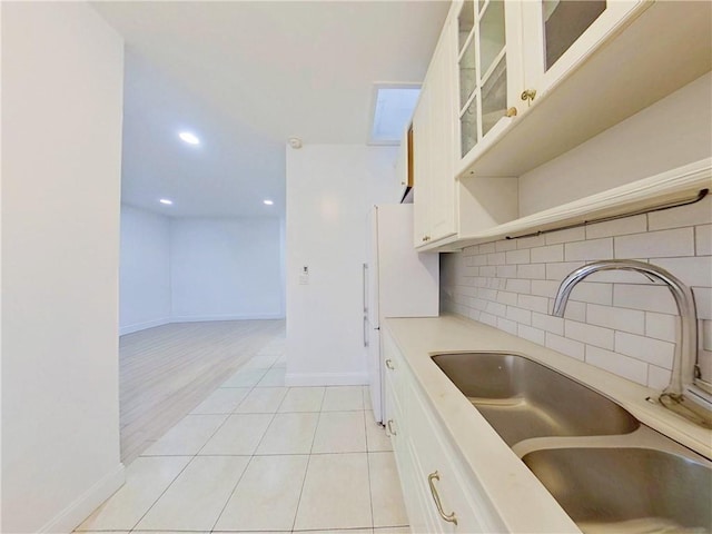 kitchen with light countertops, decorative backsplash, glass insert cabinets, white cabinetry, and a sink