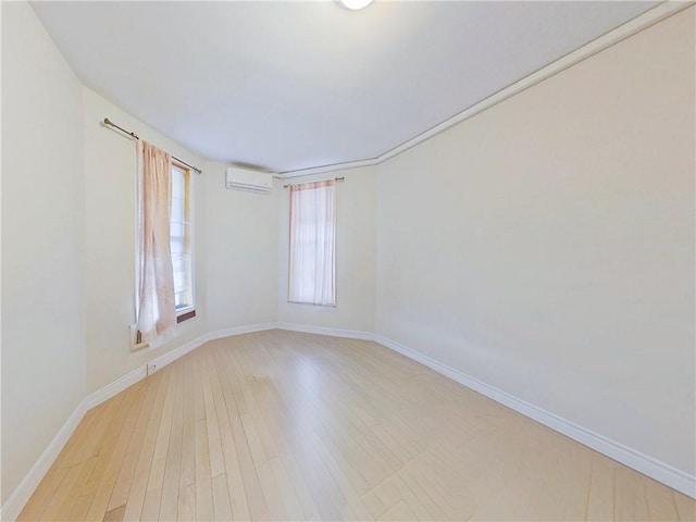 spare room featuring light wood finished floors, baseboards, and a wall mounted AC