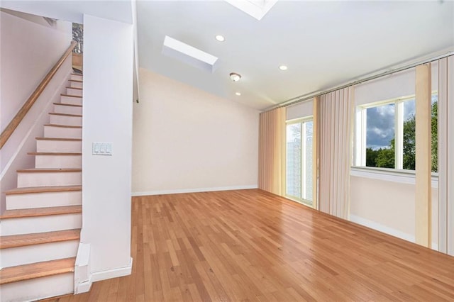 unfurnished living room featuring recessed lighting, wood finished floors, baseboards, stairway, and lofted ceiling with skylight