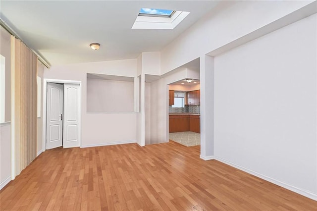 empty room with vaulted ceiling with skylight, light wood-type flooring, and baseboards