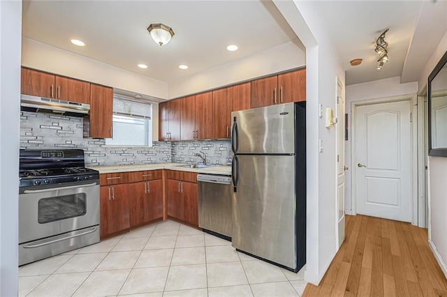 kitchen featuring stainless steel appliances, light countertops, backsplash, a sink, and under cabinet range hood