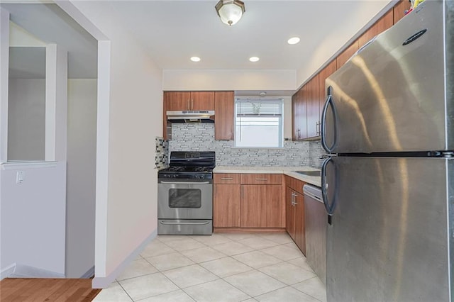 kitchen featuring stainless steel appliances, light countertops, decorative backsplash, brown cabinetry, and under cabinet range hood