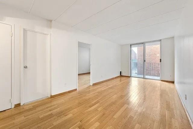 empty room with baseboards, floor to ceiling windows, and light wood finished floors