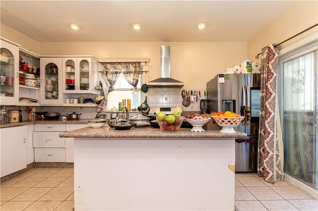 kitchen with stainless steel appliances, wall chimney range hood, light tile patterned flooring, and white cabinets