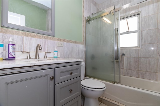 bathroom featuring combined bath / shower with glass door, toilet, tile walls, and vanity