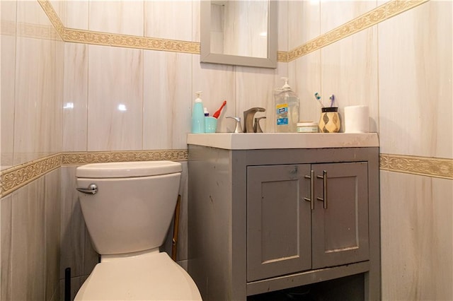 half bath featuring vanity, toilet, and tile walls