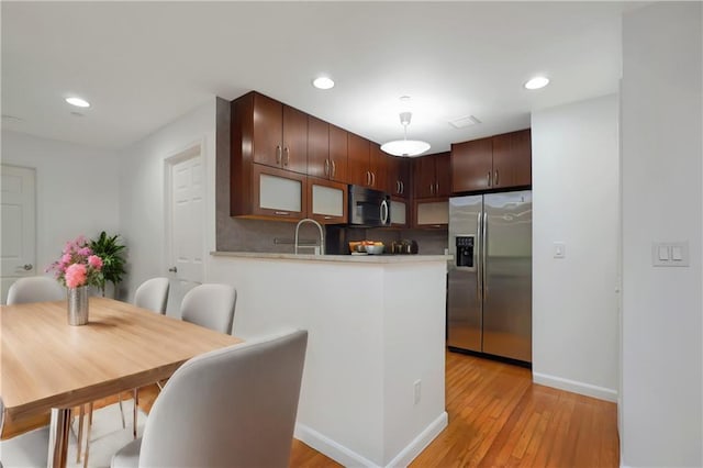 kitchen with tasteful backsplash, light wood-type flooring, light countertops, appliances with stainless steel finishes, and a peninsula