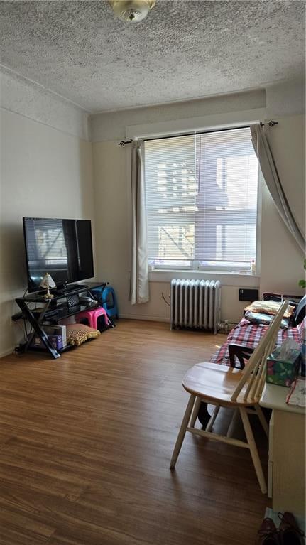 interior space with a textured ceiling, radiator heating unit, and wood finished floors