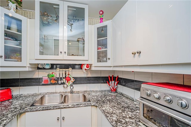 kitchen featuring decorative backsplash, glass insert cabinets, white cabinets, a sink, and range