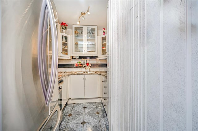 kitchen with light tile patterned floors, a sink, white cabinets, freestanding refrigerator, and glass insert cabinets