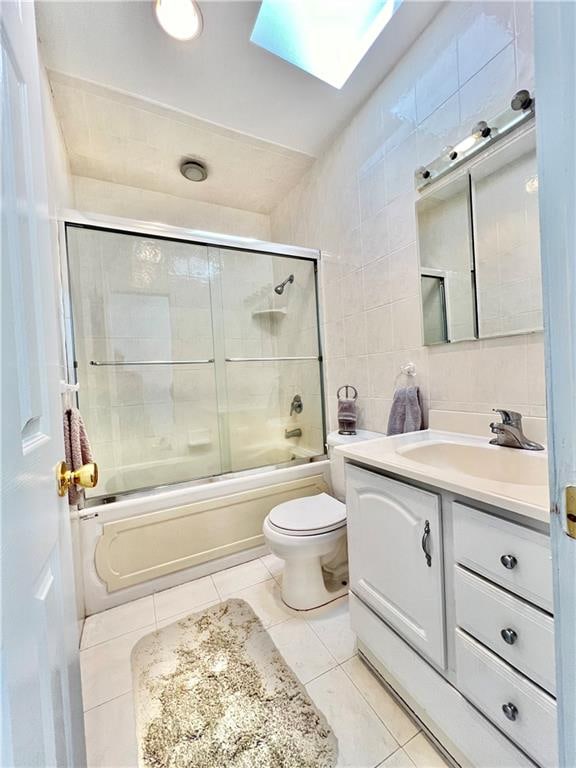 bathroom with a skylight, tile walls, bath / shower combo with glass door, vanity, and tile patterned floors