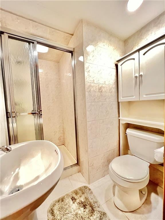 bathroom featuring a stall shower, toilet, a sink, tile patterned flooring, and tile walls