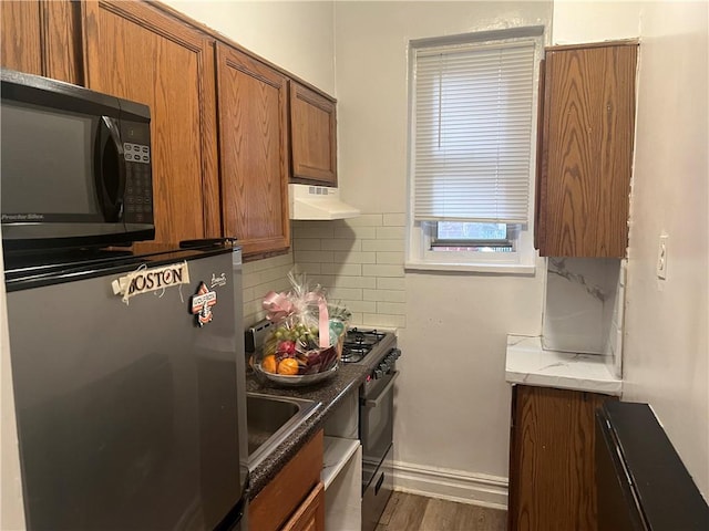 kitchen with brown cabinetry, range with gas cooktop, refrigerator, under cabinet range hood, and black microwave