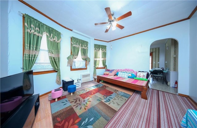 bedroom with arched walkways, crown molding, radiator, a ceiling fan, and baseboards