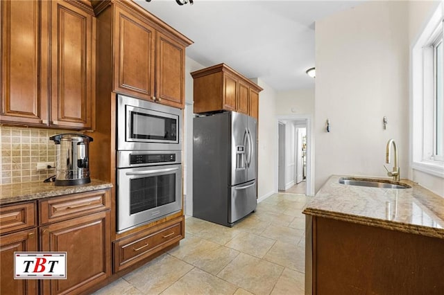 kitchen with stainless steel appliances, a sink, light stone counters, and decorative backsplash