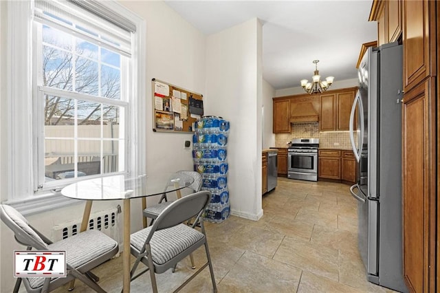 kitchen featuring a chandelier, appliances with stainless steel finishes, backsplash, brown cabinets, and stone finish flooring