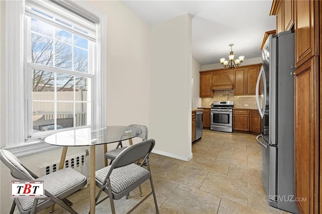 kitchen featuring appliances with stainless steel finishes, brown cabinetry, a chandelier, decorative backsplash, and baseboards