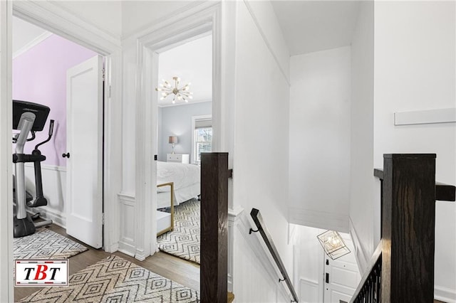 hall with an upstairs landing, wood finished floors, and a chandelier