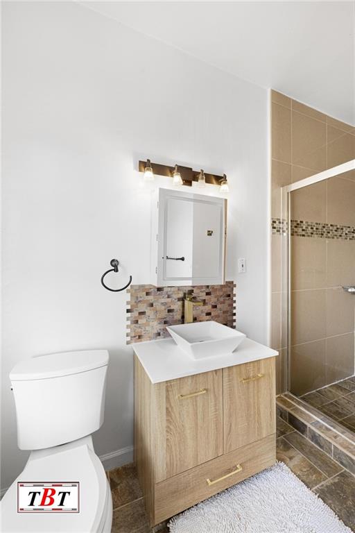 bathroom featuring toilet, tile patterned floors, vanity, a shower stall, and backsplash