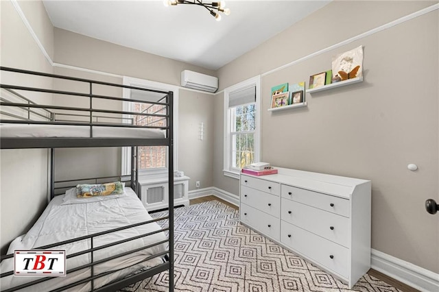 bedroom with an AC wall unit, baseboards, and light wood-style flooring