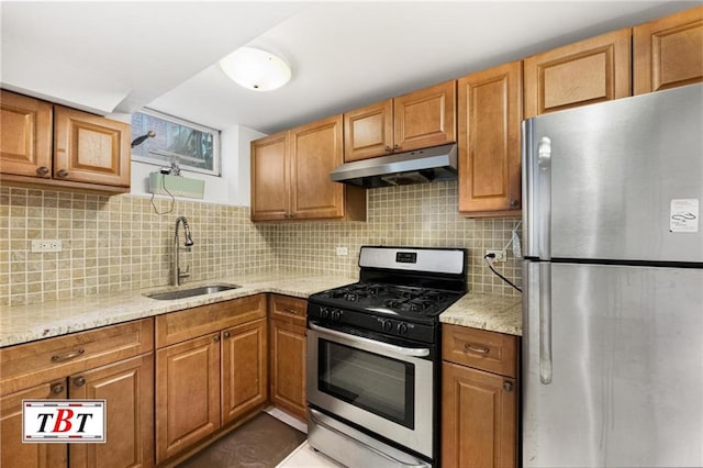 kitchen with light stone counters, under cabinet range hood, stainless steel appliances, a sink, and tasteful backsplash