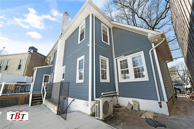 view of side of home with a cooling unit, a chimney, a deck, and fence