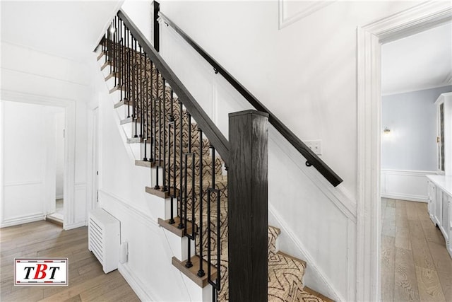 stairway featuring wood-type flooring, ornamental molding, and a decorative wall