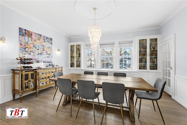 dining space with crown molding, wainscoting, a notable chandelier, and wood finished floors