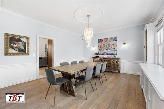dining space with a chandelier, crown molding, light wood-style floors, a wainscoted wall, and a decorative wall