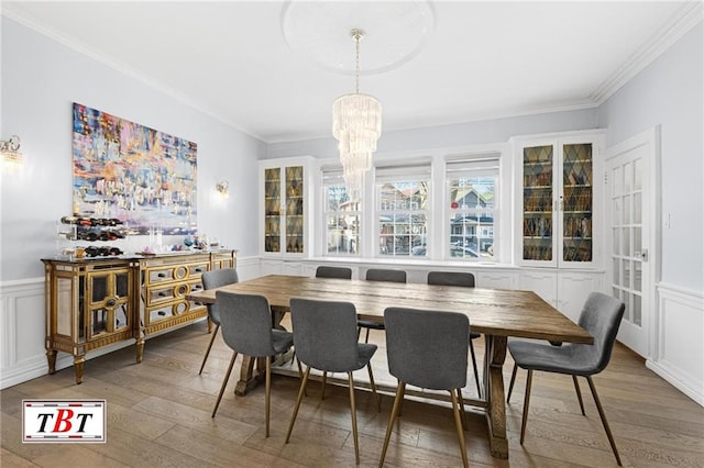 dining room featuring a chandelier, a decorative wall, wood finished floors, crown molding, and a wainscoted wall
