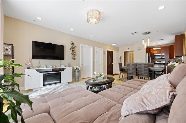 living room featuring baseboards, visible vents, a glass covered fireplace, and recessed lighting