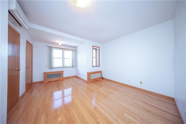 empty room with radiator, light wood finished floors, baseboards, and a wall mounted air conditioner