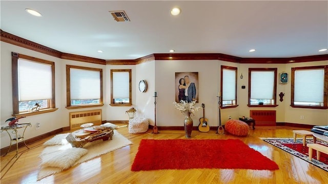 workout area with baseboards, visible vents, radiator, ornamental molding, and wood finished floors