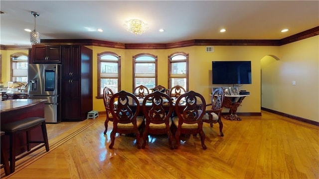 dining room featuring light wood finished floors, baseboards, arched walkways, ornamental molding, and recessed lighting