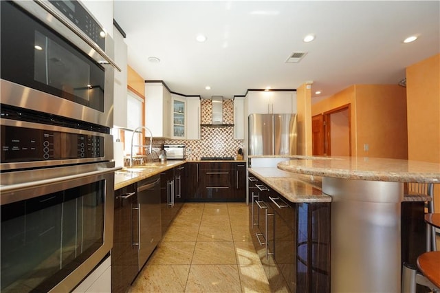 kitchen featuring stainless steel appliances, visible vents, wall chimney range hood, tasteful backsplash, and a kitchen bar