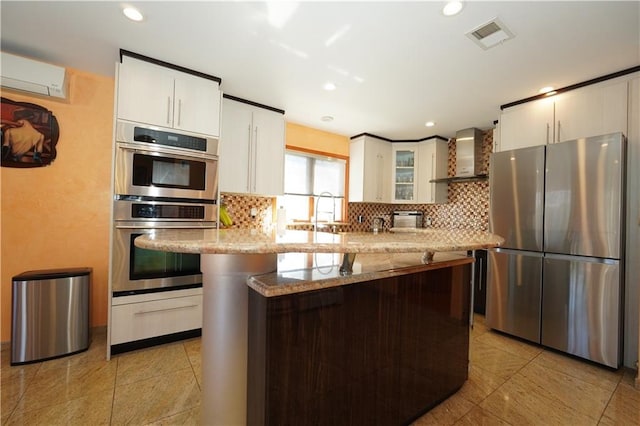 kitchen with a wall unit AC, wall chimney range hood, appliances with stainless steel finishes, and backsplash