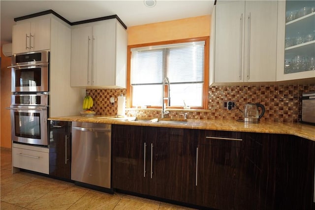 kitchen with stainless steel appliances, a sink, dark brown cabinets, tasteful backsplash, and glass insert cabinets