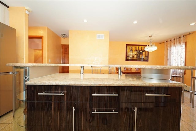 kitchen featuring recessed lighting, visible vents, dark brown cabinets, and an island with sink