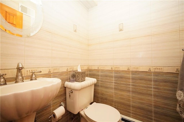 half bath featuring a sink, toilet, and tile walls