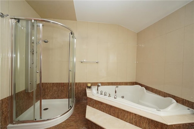 bathroom with a garden tub, a shower stall, vaulted ceiling, and tile walls