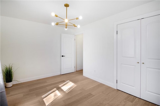 unfurnished bedroom featuring a closet, light wood-style flooring, baseboards, and an inviting chandelier