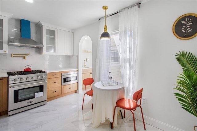 kitchen featuring backsplash, stainless steel appliances, light countertops, wall chimney range hood, and a sink