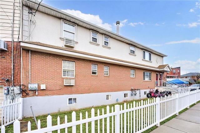 view of home's exterior with a wall unit AC, fence, brick siding, and stucco siding