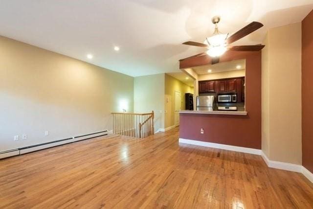 unfurnished living room with recessed lighting, baseboard heating, light wood-style floors, a ceiling fan, and baseboards