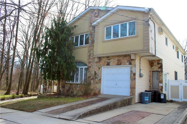 view of front of home featuring a garage, driveway, stone siding, fence, and stucco siding