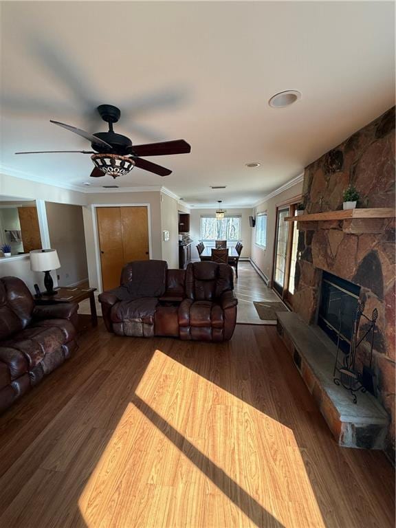 living area with a stone fireplace, wood finished floors, a ceiling fan, and crown molding